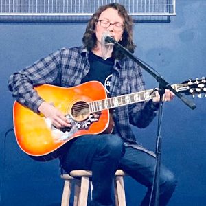 Artist performs with acoustic guitar in front of a blue wall.
